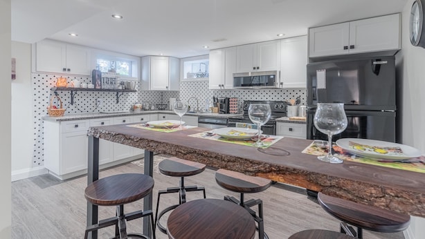A modern kitchen with white cabinets, a central island with stools, a refrigerator, and a microwave.