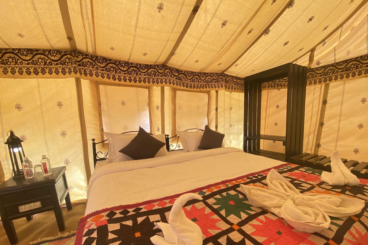 Habitación de hotel con cama, almohadas, mesita de noche, lámpara y colcha con diseños de cisnes.