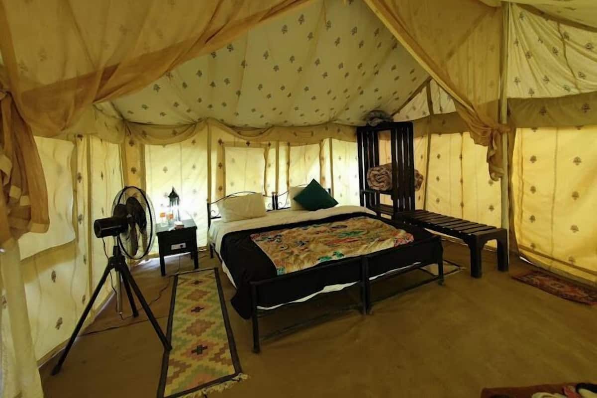 Una habitación tipo tienda de campaña con una cama, un ventilador, una mesita pequeña y un banco.