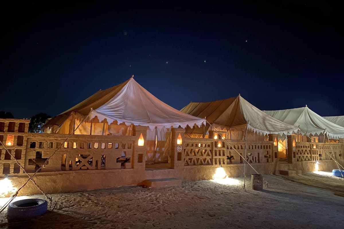 Un campamento en el desierto con tiendas de campaña y un edificio de piedra con múltiples ventanas y una escalera.
