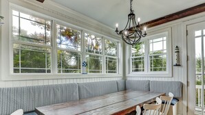 A large wooden dining table with white chairs, a built-in bench with patterned cushions, and a chandelier. - North Beach Tybee Home With Roof Top Deck | Walk to Beach | Heated pool access (Tybee Island)