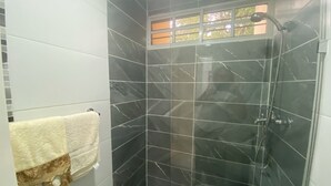 Ein Badezimmer mit dunklen Marmorfliesen, einer Duschkabine aus Glas und einem Fenster mit Blick.