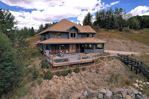 A two-story house with a deck, surrounded by natural landscape.