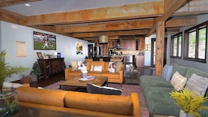 A spacious living area with a large sofa, a coffee table, and a dining area with wooden cabinets and a kitchen in the background. - Whetstone Wonder, Views! Pet Friendly, Hot tub (Mt. Crested Butte)