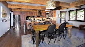 A spacious kitchen with wooden cabinets, a dining area with a wooden table and chairs, and a large window providing natural light. - Whetstone Wonder, Views! Pet Friendly, Hot tub (Mt. Crested Butte)