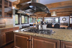 Une cuisine dotée de plans de travail en granit, de meubles en bois, d’une cuisinière en acier inoxydable et d’une grande fenêtre donnant sur un paysage pittoresque.
