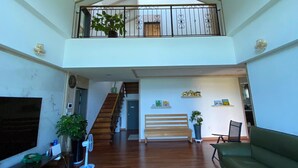 Un amplio salón con una escalera de madera, un balcón con barandilla y un sofá verde.