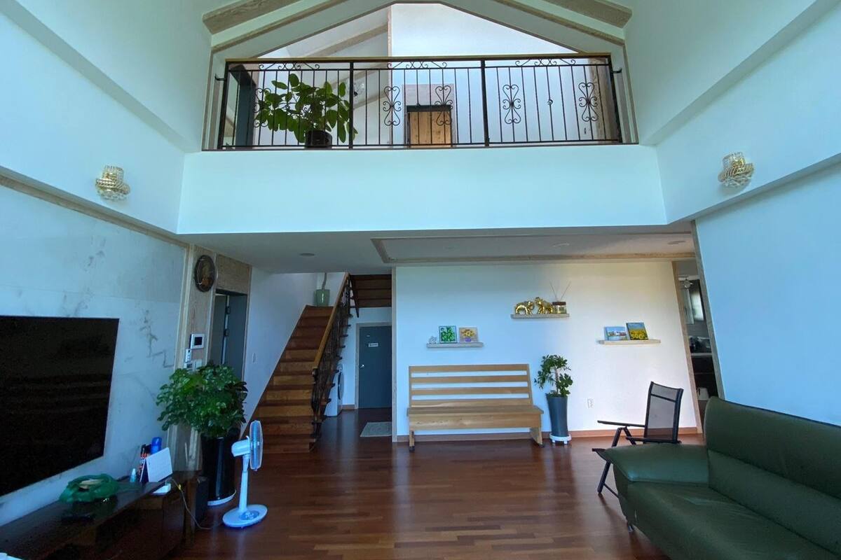 Un vaste espace de vie agrémenté d’un escalier en bois, d’un balcon avec une balustrade et d’un canapé vert.