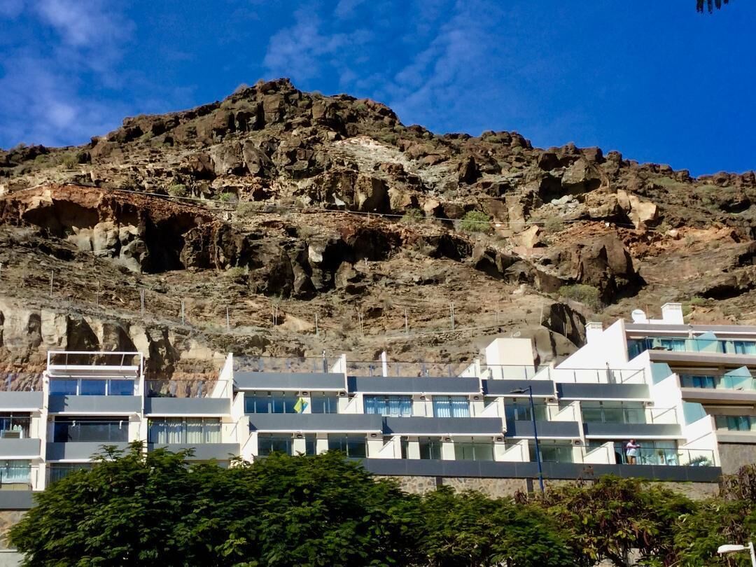 A coastal hotel with modern architecture, featuring multiple balconies and a view of rocky cliffs.