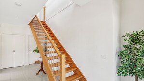 A wooden staircase in a modern interior with white walls and a potted plant. - Beach View Escape - Close to the Beach & WiFi (Safety Beach)