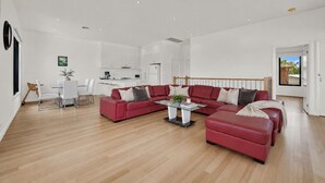 A spacious living area with a red sectional sofa, a dining table with chairs, and a kitchen in the background. - Beach View Escape - Close to the Beach & WiFi (Safety Beach)