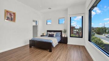 A bedroom with a large window, a bed, a nightstand, and a framed picture on the wall.