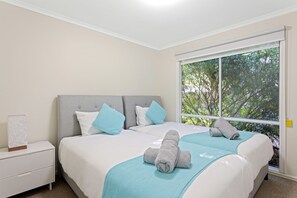 A bedroom with a large window, a bed with a grey headboard, and a nightstand with a lamp. - Bethel by the Sea by Ready Set Stay - Close to the beach & WiFi (Surf Beach)