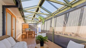 Een zonnig terras met houten meubels, een tafel en plantenpotten.