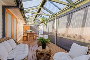 A sunlit patio with wooden furniture, a table, and potted plants. - Bethel by the Sea by Ready Set Stay - Close to the beach & WiFi (Surf Beach)