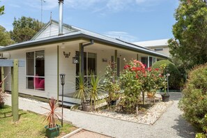 A single-story building with a covered porch, a visible chimney, and a garden area with various plants and flowers. - Bethel by the Sea by Ready Set Stay - Close to the beach & WiFi (Surf Beach)