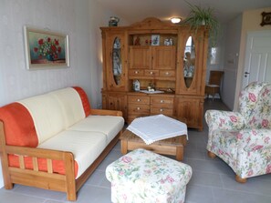 Una sala de estar con un sofá, dos sillones, un aparador de madera y un cuadro en la pared.