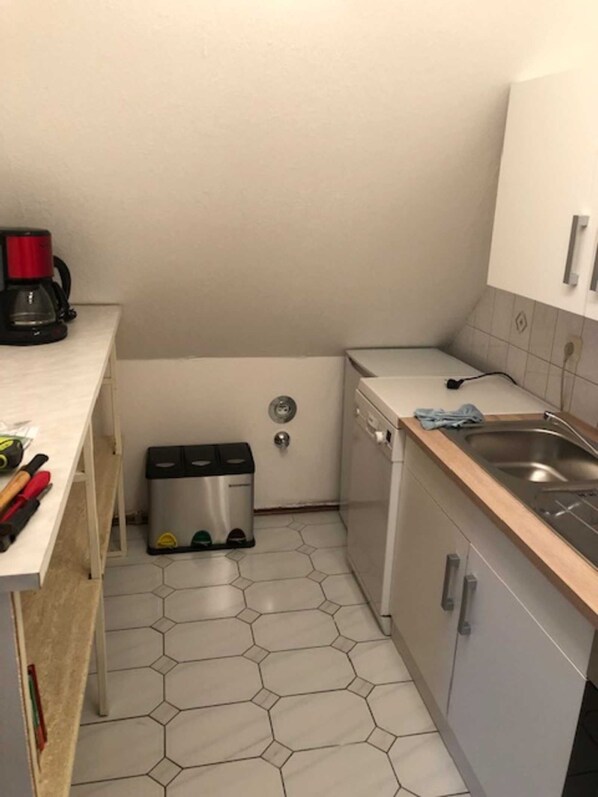 Une cuisine compacte équipée d’une machine à café, d’une poubelle et d’un lave-vaisselle.