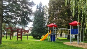 Ein Spielplatz mit einer roten und gelben Rutsche, Klettergerüsten und einem Spielhäuschen mit rotem Dach.