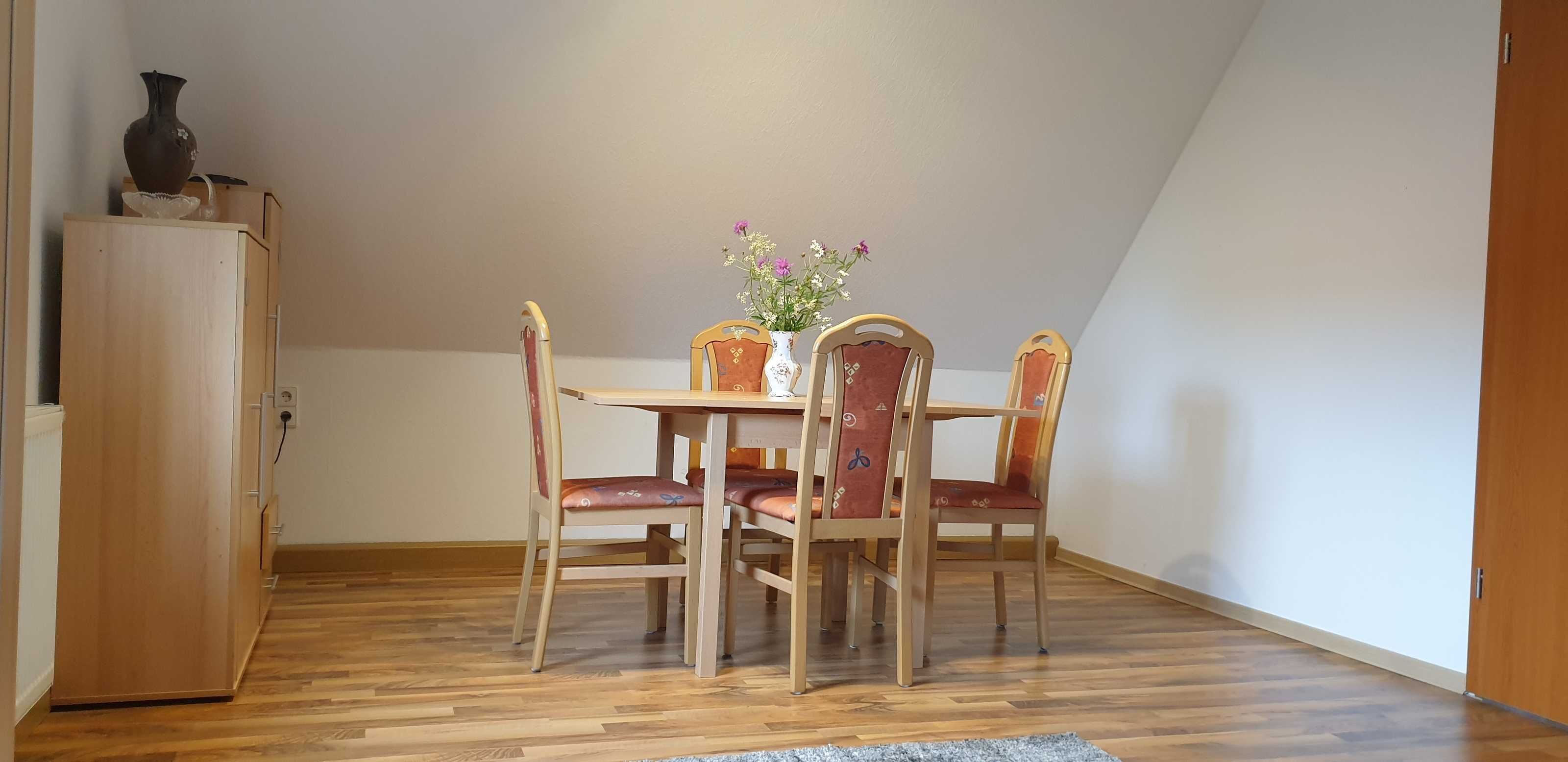 A dining area with a wooden table and four chairs, a vase with flowers, and a cabinet.