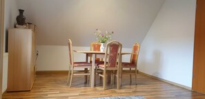 A dining area with a wooden table and four chairs, a vase with flowers, and a cabinet.