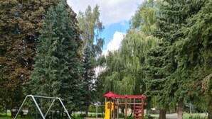 Ein Spielplatz mit Schaukeln, einer Rutsche und Picknicktischen in einer grünen Parkanlage.