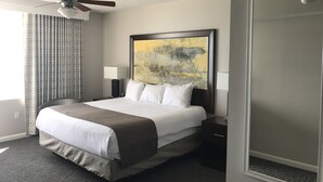 Habitación de hotel con una cama grande, ventilador de techo, un cuadro en la pared y ventana con cortinas.