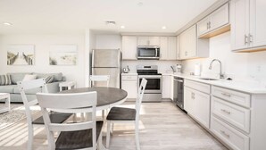 A modern kitchen with white cabinetry, a built-in oven, microwave, and dishwasher. There is a dining area with a round table and chairs.