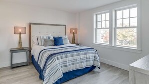 A bedroom with a bed, two bedside tables, two lamps, and a window with a view of the outside.