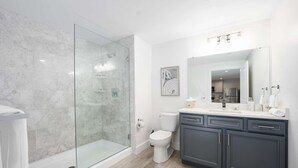 A modern bathroom with a glass-enclosed shower, a toilet, and a vanity with a mirror.