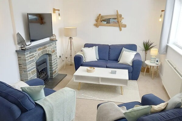A living room with a stone fireplace, a blue sofa, a white coffee table, and a television mounted above the fireplace.