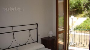 A bedroom with a bed, a nightstand with a lamp, and a sliding glass door leading to an outdoor area. - Holiday Home Residence "i delfini" (Badesi)