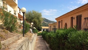 A narrow stone pathway flanked by greenery and buildings with balconies and traditional architecture. - Holiday Home Residence "i delfini" (Badesi)