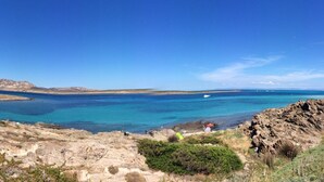 A coastal landscape with rocky terrain, clear blue waters, and a distant island. - Holiday Home Residence "i delfini" (Badesi)