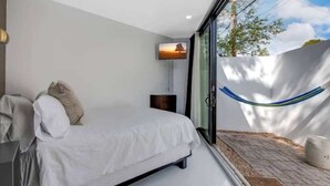 Un dormitorio moderno con una cama, un televisor montado en la pared y vistas al exterior a través de un ventanal.