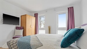 Ein Schlafzimmer mit einem Bett, einem Schrank, einem Fernseher und zwei mit Vorhängen versehenen Fenstern.