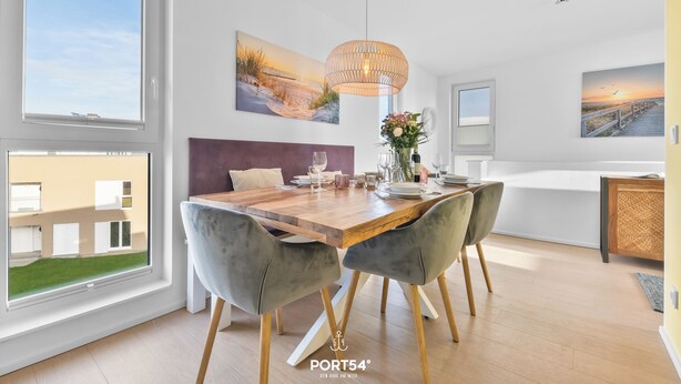 A modern dining area with a wooden table, grey upholstered chairs, and a hanging light fixture. - Wolke 7 - Infrared Sauna, Fireplace, Rooftop Terrace, Bathtub, Parking Space (Olpenitz)