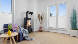 A modern living room with a wood-burning stove, a blue sofa, a small round table with a yellow vase, and large windows. - Wolke 7 - Infrared Sauna, Fireplace, Rooftop Terrace, Bathtub, Parking Space (Olpenitz)