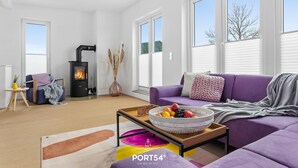 A modern living room with a sofa, a coffee table with a fruit bowl, a fireplace, and large windows. - Wolke 7 - Infrared Sauna, Fireplace, Rooftop Terrace, Bathtub, Parking Space (Olpenitz)