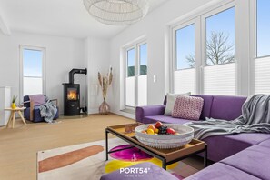 Ein modernes Wohnzimmer mit einer Couch, einem Couchtisch mit Obstschale, einem Kamin und großen Fenstern.