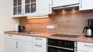 Une cuisine moderne avec des meubles blancs, un plan de travail en bois, un four encastré et une machine à café.