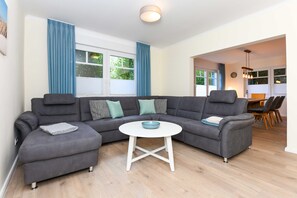 Un salon moderne avec un canapé d’angle, une table basse ronde et un coin repas à l’arrière-plan.