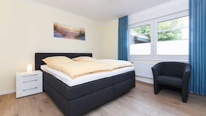 Une chambre à coucher avec un lit, une table de chevet, une chaise et une fenêtre avec des rideaux.