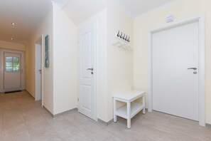 Un couloir avec deux portes blanches, un petit banc blanc et un porte-manteau.