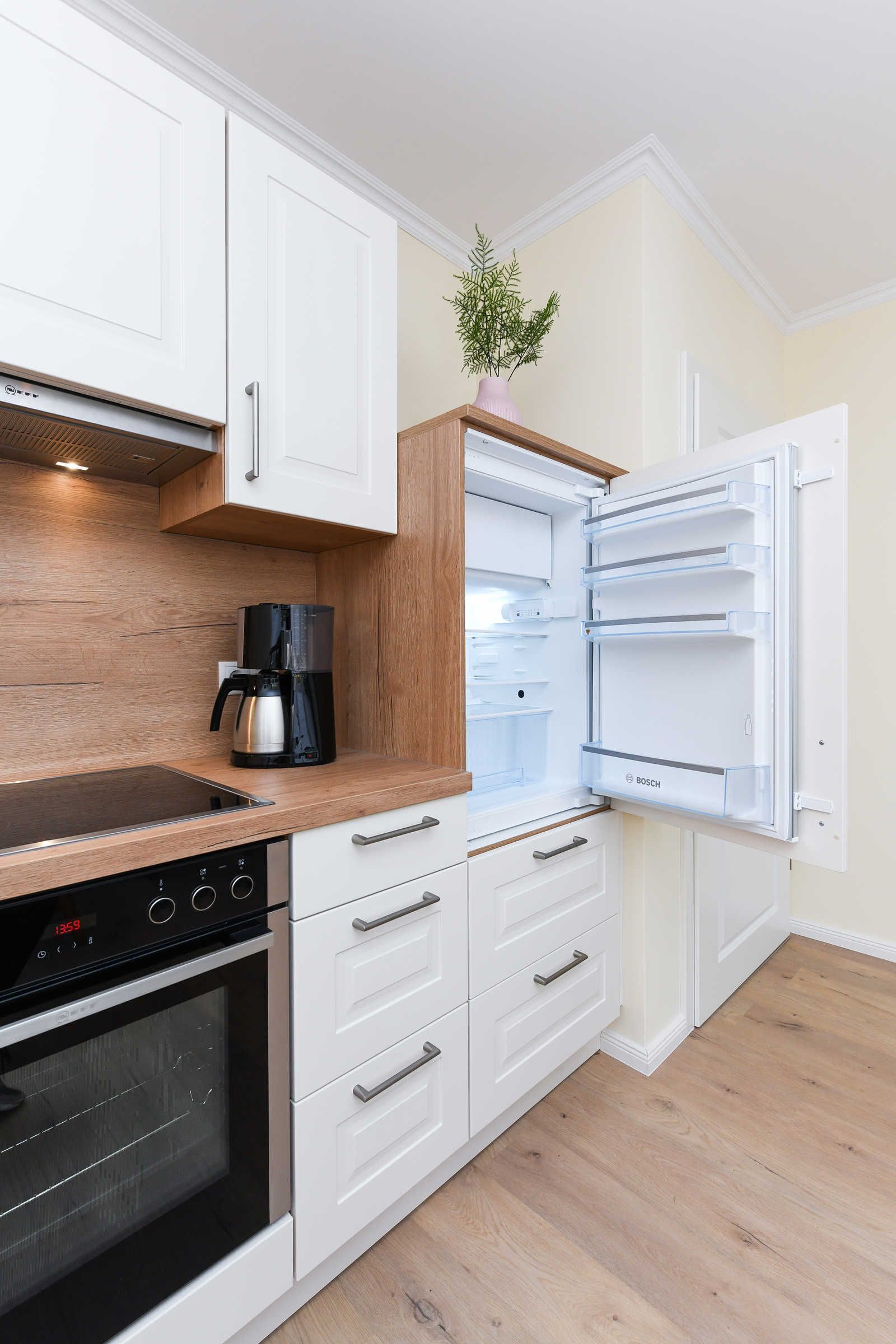 A modern kitchen with white cabinetry, a built-in oven, a coffee maker, and a Bosch refrigerator.