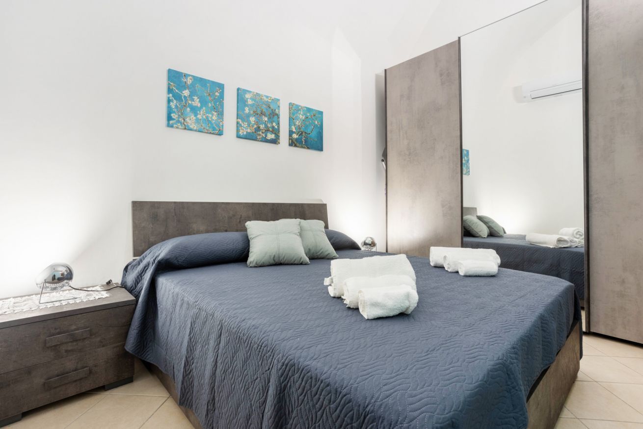 A modern bedroom with a large bed, two pillows, a bedside table, and a mirror.