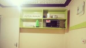 A kitchen with a gas stove, a microwave, and shelves above containing jars, plates, and kitchen utensils. - smiles home (Thika)