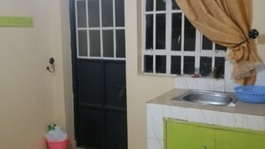 A small kitchen with a sink, green cabinets, a window with a curtain, and a door. - smiles home (Thika)