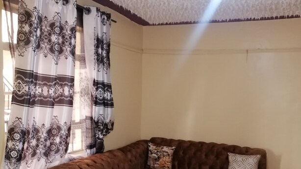 A living room with a brown sectional sofa, a small ottoman, and a remote control on the ottoman. - smiles home (Thika)