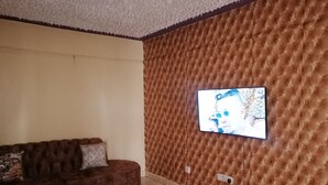 A living room with a brown tufted wall, a brown sofa, and a television mounted on the wall. - smiles home (Thika)